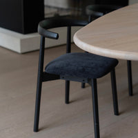 t4option0_3 | Ella dining chair by Mowelli with a upholstered seat and wooden backrest, all black, around a table, fireplace in the back.