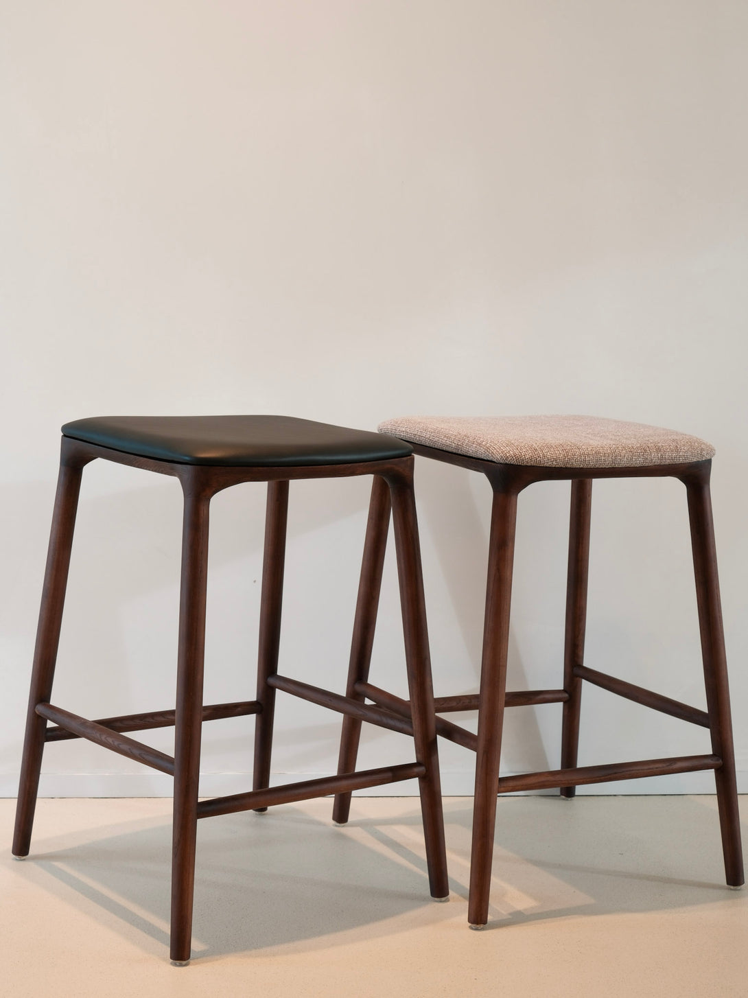 Two Mowelli bar stools in dark walnut wood with fabric upholstered and leather seats