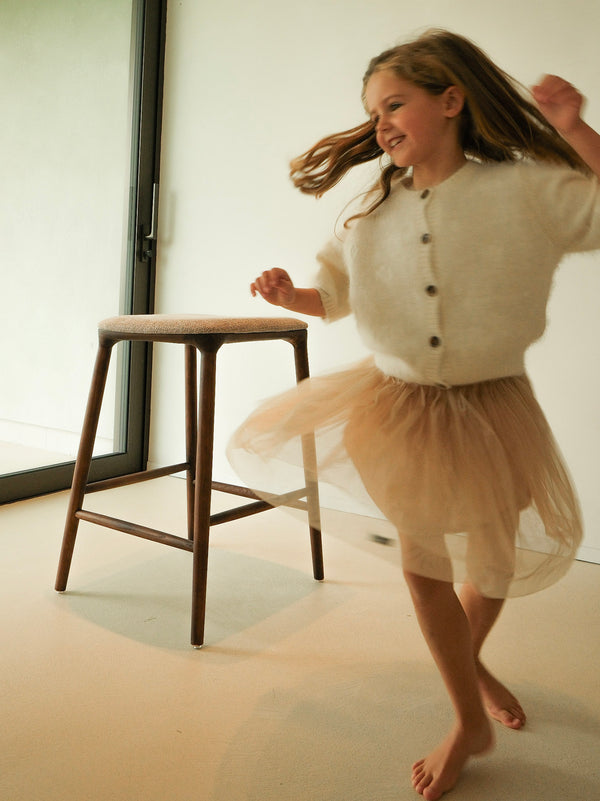 Child sitting on a Mowelli bar stool with wooden legs and upholstered seat in cozy home setting