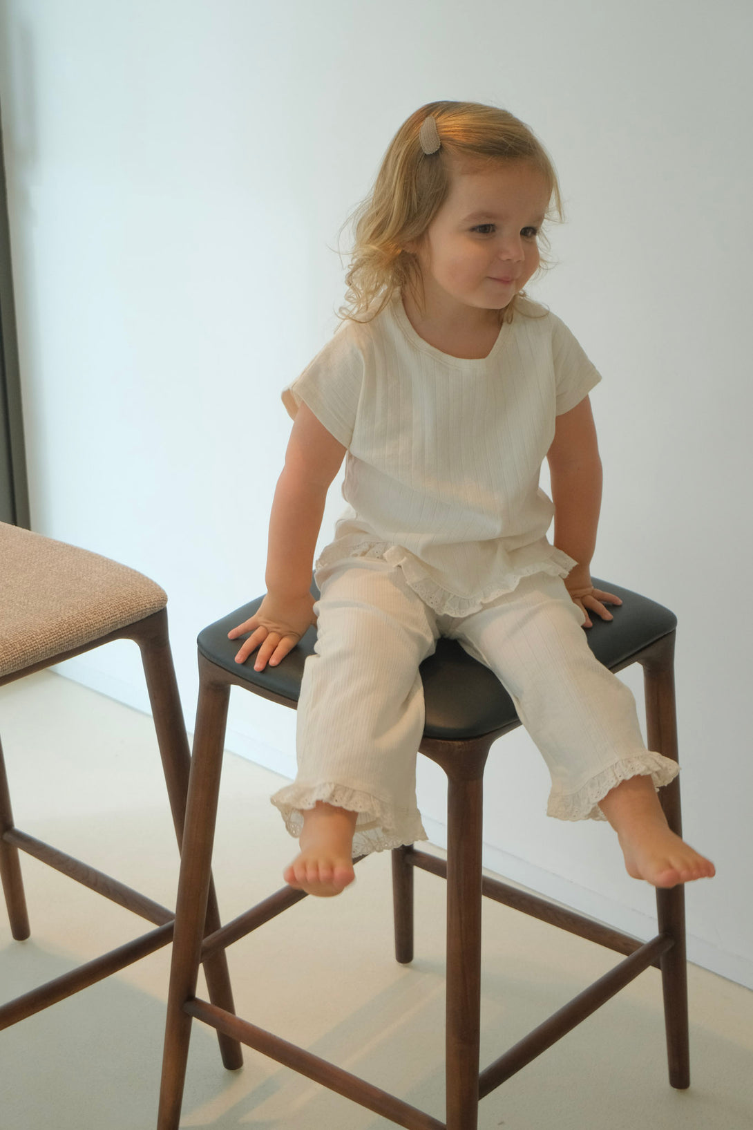 Child sitting on Mowelli bar stool with black leather seat, walnut wood frame, minimalist Belgian design