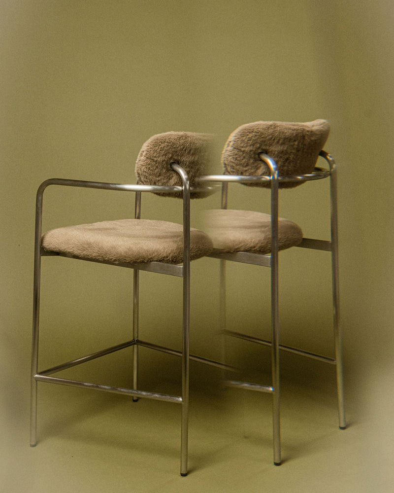 Coco bar chair in sage grey textured upholstery with a brushed stainless steel frame, shown in a minimal interior setting