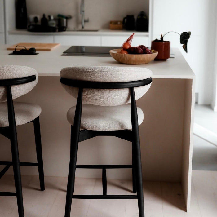 Pair of Mowelli Dianne bar stools with black wooden frame and light beige upholstery at a modern kitchen counter