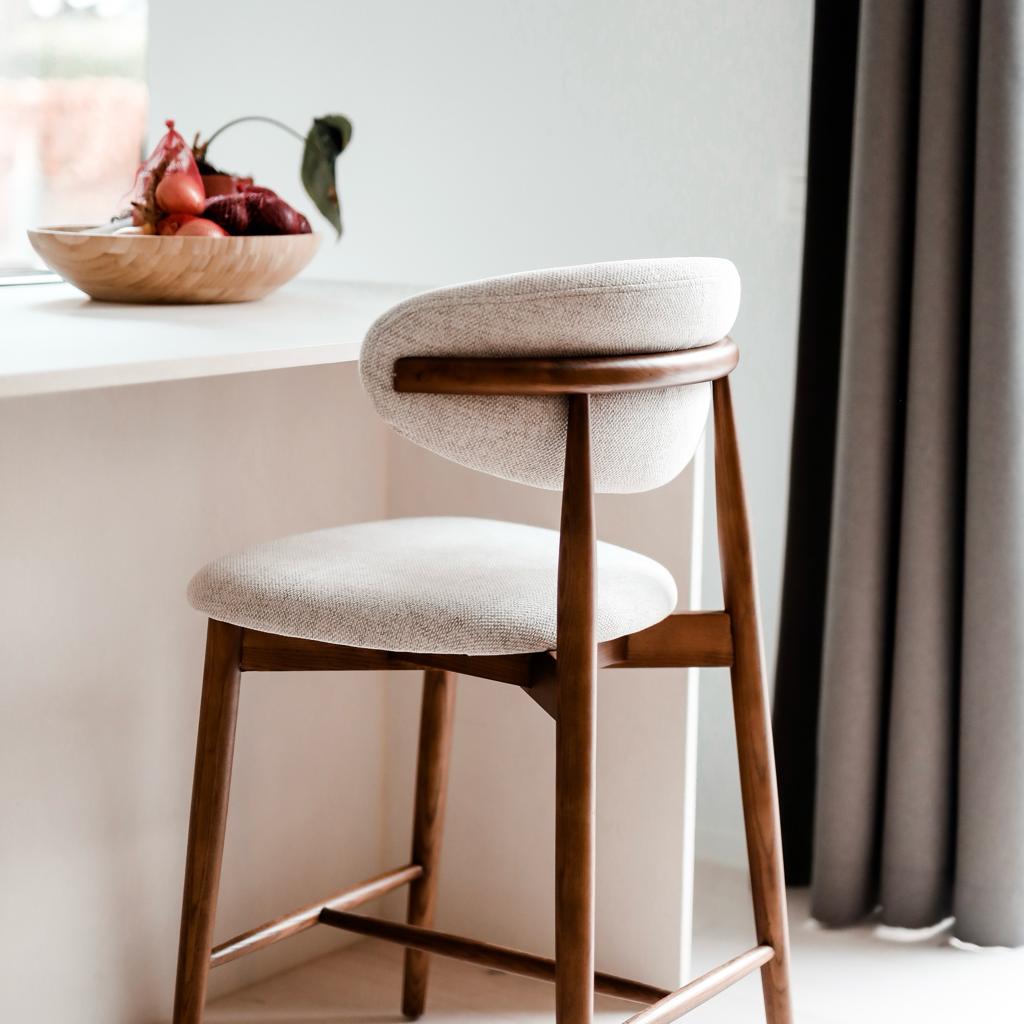 Side profile of the Mowelli Dianne bar stool in walnut wood with curved back and eco-friendly fabric