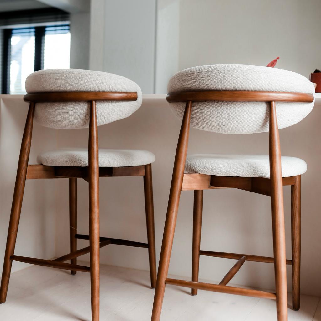 Back view of walnut Mowelli Dianne bar stools with soft beige upholstery and Scandinavian lines