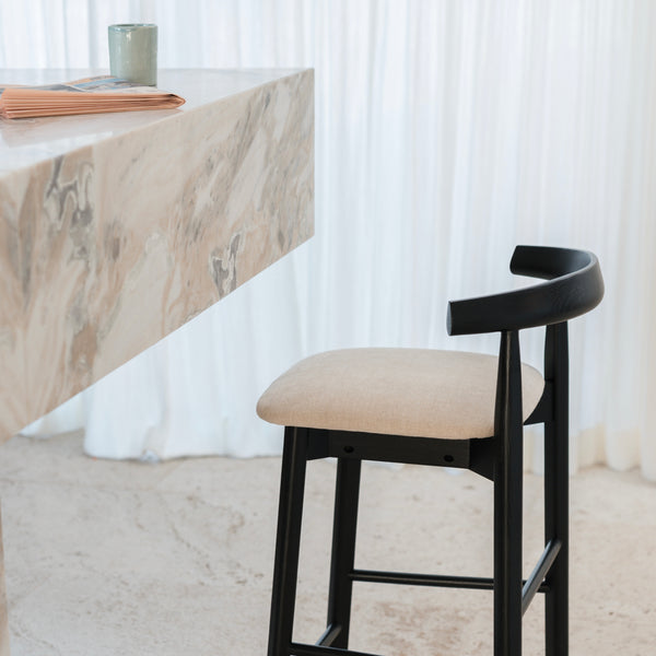Side view of black Ella bar stool by Mowelli with beige seat, positioned at a marble kitchen counter.