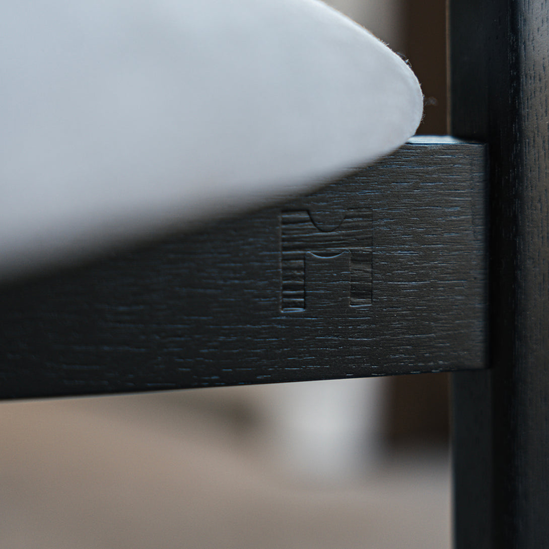 Detail of Mowelli logo engraved in black wood frame of Ella bar stool beneath upholstered seat.