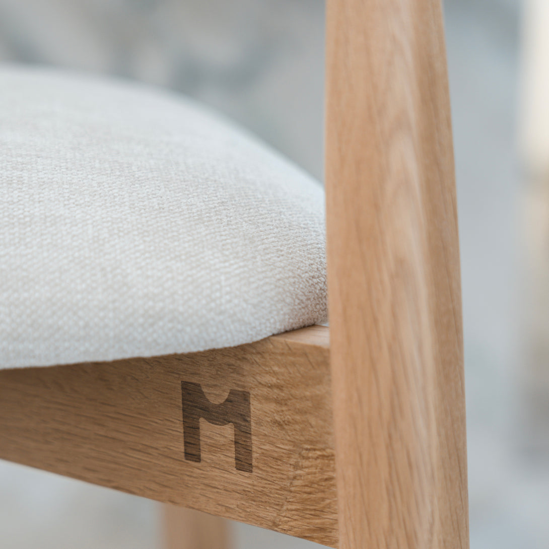 Detail of light oak Ella bar stool by Mowelli with engraved M logo beneath upholstered seat.