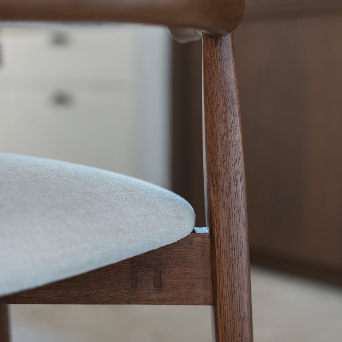 Close-up of Ella bar stool by Mowelli in walnut wood with beige upholstered seat and engraved logo detail.