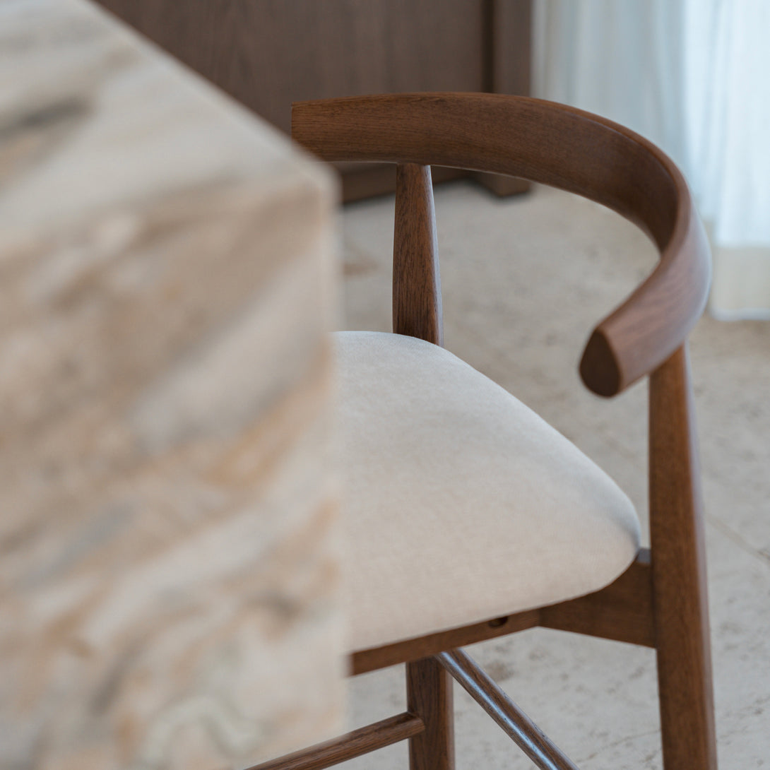 Angled view of Ella bar stool by Mowelli in walnut finish with curved backrest and beige seat.