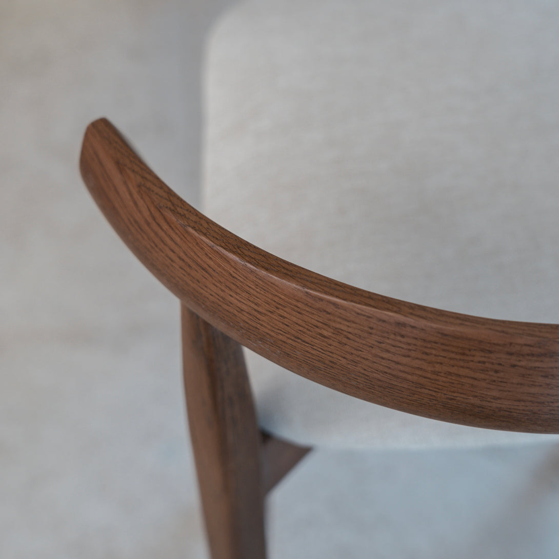 Close-up of curved walnut wood backrest on Ella bar stool by Mowelli with beige fabric seat.