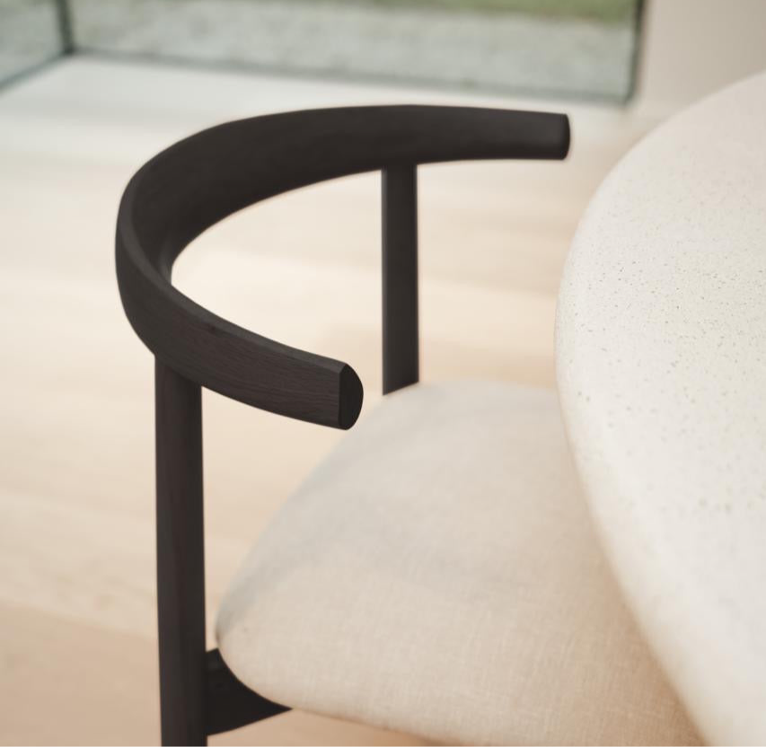 Close-up of black oak Ella dining chair by Mowelli with off-white seat, near dining table.