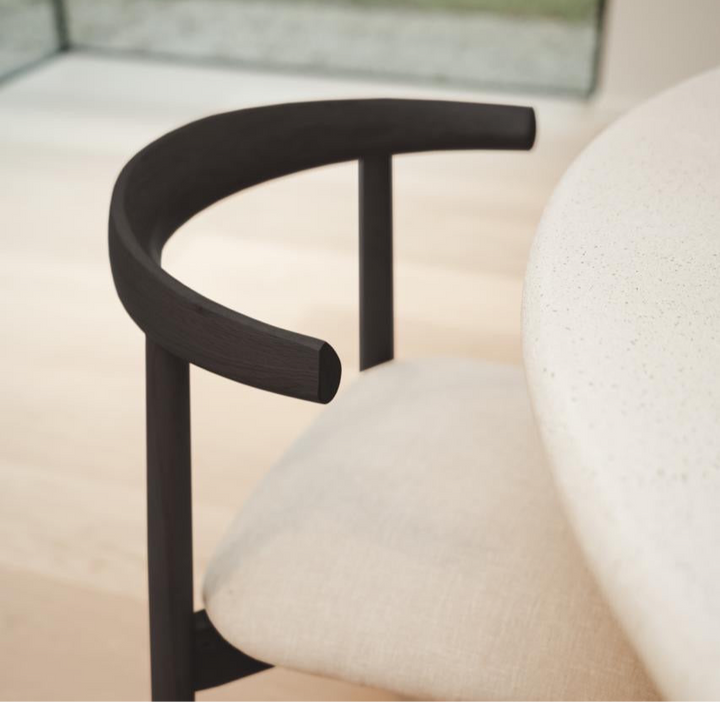 Close-up of black oak Ella dining chair by Mowelli with off-white seat, near dining table.