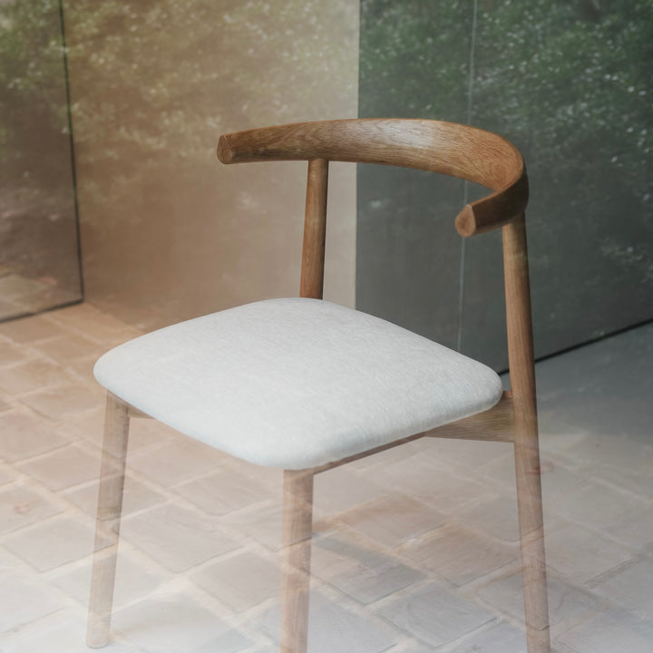 Minimalist interior featuring Ella dining chair by Mowelli in natural oak and cosy fabric seat, placed by a window.