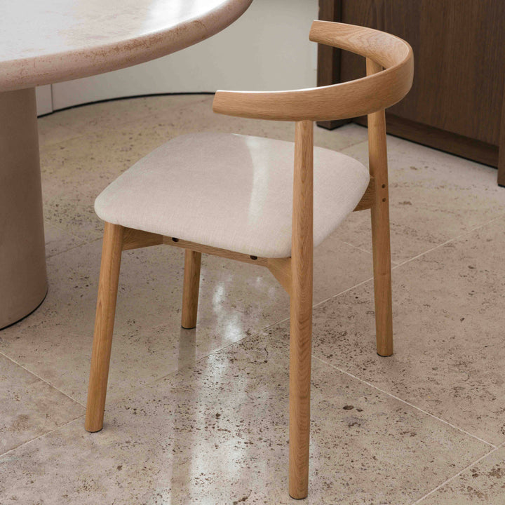 Close-up of Ella dining chair by Mowelli in natural oak with beige upholstered seat on natural stone floor