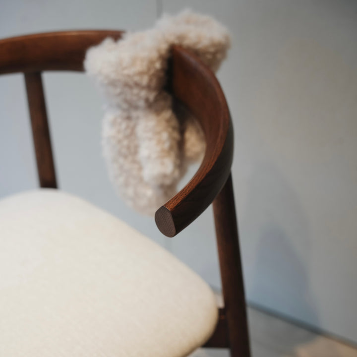 Detail of Ella dining chair by Mowelli in dark walnut with curved backrest and cream fabric seat.
