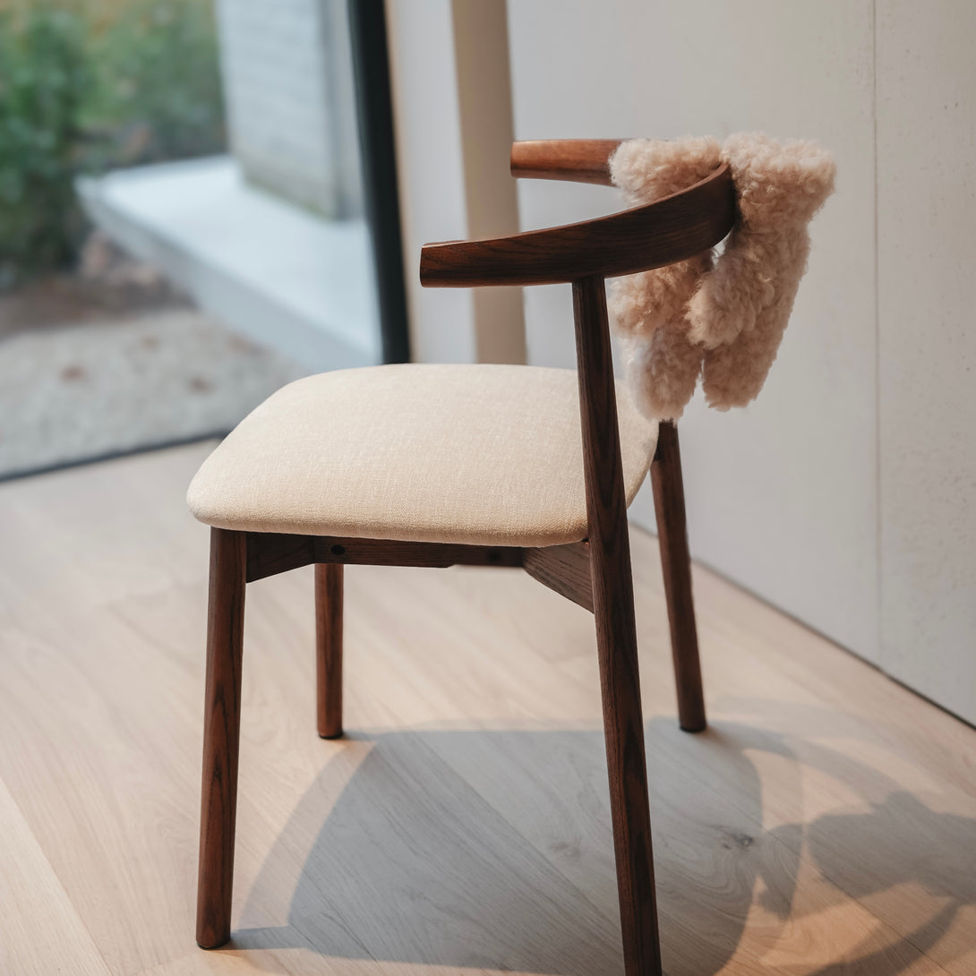 Ella dining chair by Mowelli in walnut wood with beige cushion, softly lit interior scene.