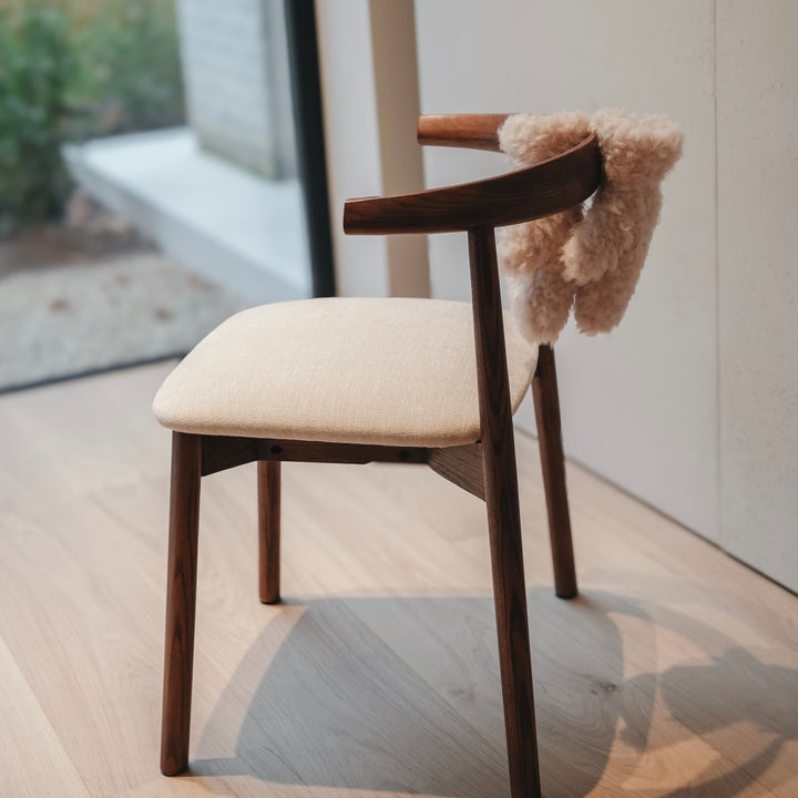 Ella dining chair by Mowelli in walnut wood with beige cushion, softly lit interior scene.