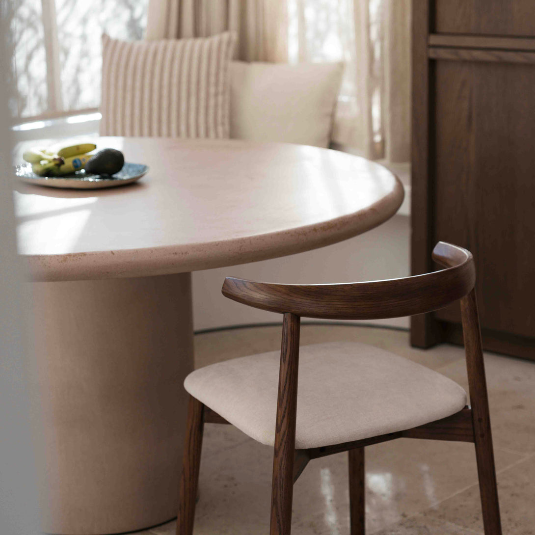 Ella dining chair by Mowelli in walnut wood next to round dining table with light fabric seat