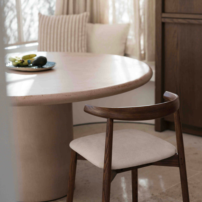 Ella dining chair by Mowelli in walnut wood next to round dining table with light fabric seat