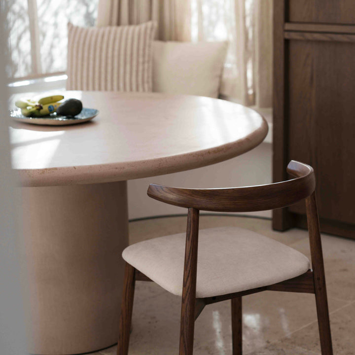 Ella dining chair by Mowelli in walnut wood next to round dining table with light fabric seat