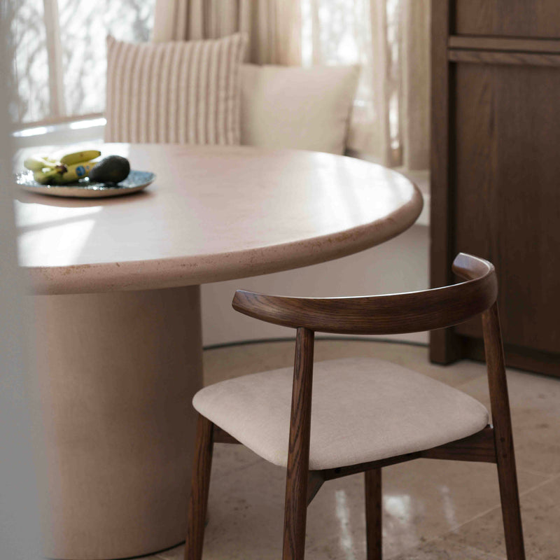 Ella dining chair by Mowelli in walnut wood next to round dining table with light fabric seat