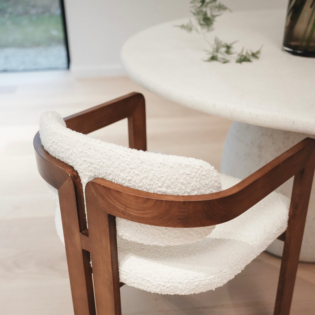 Close-up back view of Mila chair by Mowelli showing the white bouclé fabric backrest and seat, with armrest made out of ash wood in walnut colour