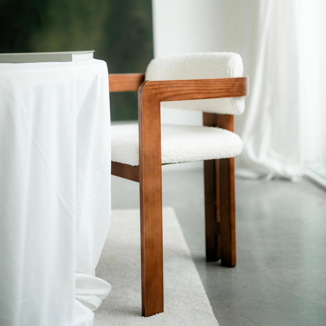 Angled view of Mila chair by Mowelli with a detailed look on walnut armrest, standing at a white table