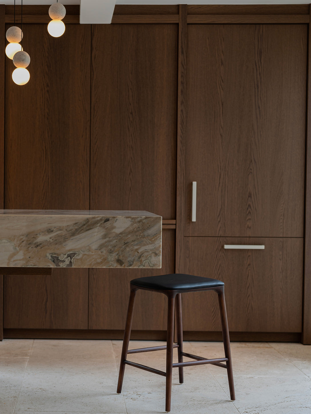 Mowelli Nora counter stool in brown walnut wood with premium vegan leather upholstered seat and minimalist backless design.