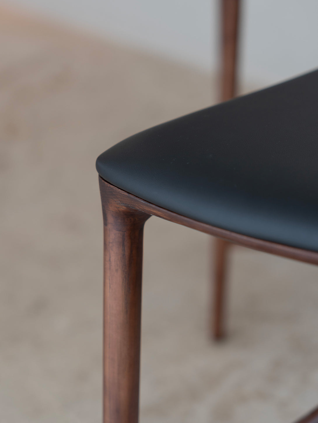 Mowelli Nora counter stool in brown walnut wood with premium vegan leather upholstered seat and minimalist backless design.