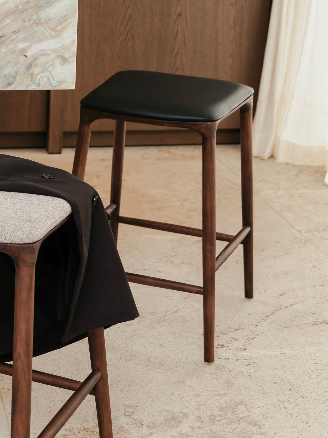 Mowelli Nora counter stool in brown walnut wood with premium vegan leather upholstered seat and minimalist backless design.