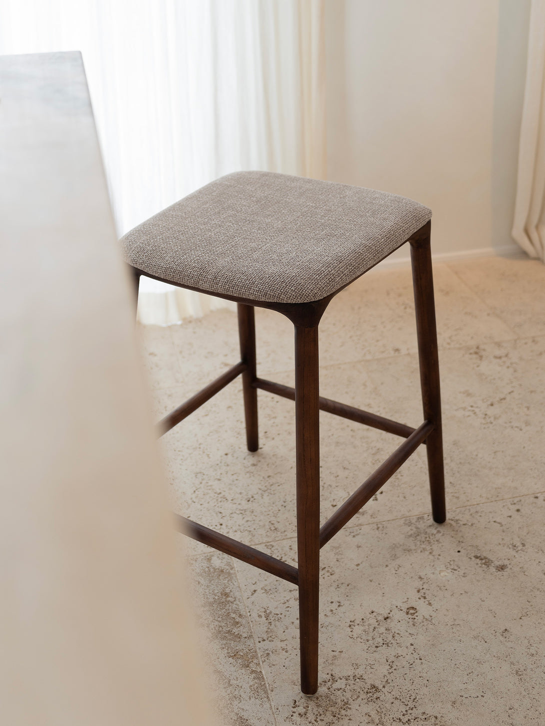 Mowelli Nora counter stool – stylish backless counterstool in brown walnut with soft upholstered cushion seat, ideal for kitchen counters and modern interiors.