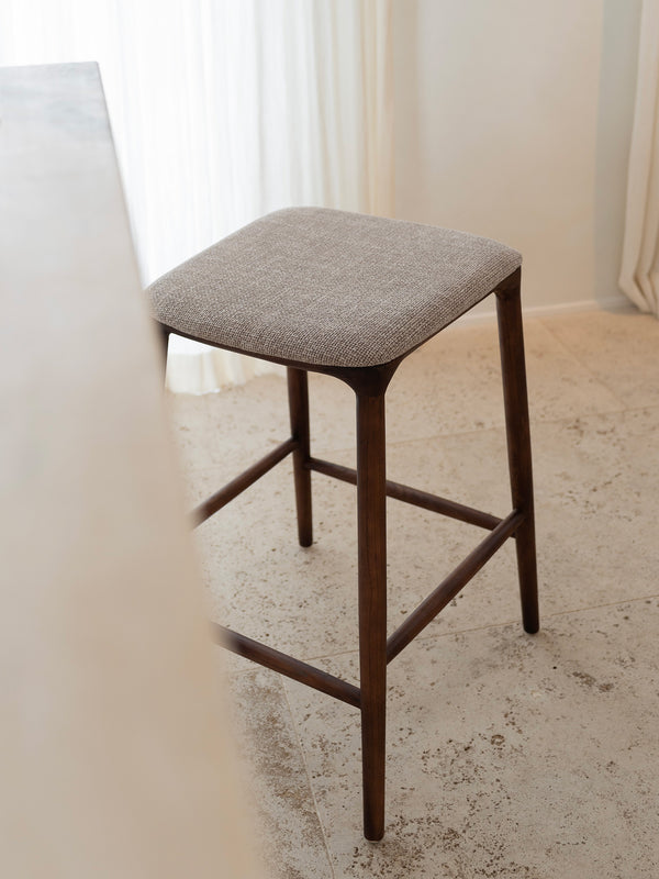 Mowelli Nora counter stool – stylish backless counterstool in brown walnut with soft upholstered cushion seat, ideal for kitchen counters and modern interiors.
