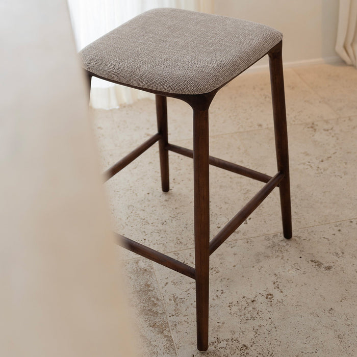 Mowelli Nora counter stool – stylish backless counterstool in brown walnut with soft upholstered cushion seat, ideal for kitchen counters and modern interiors.