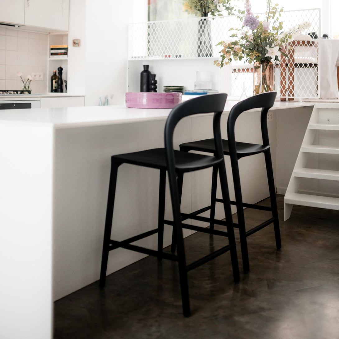 Two black Nora bar stools by Mowelli placed at a modern white kitchen island – sustainable European bar chairs