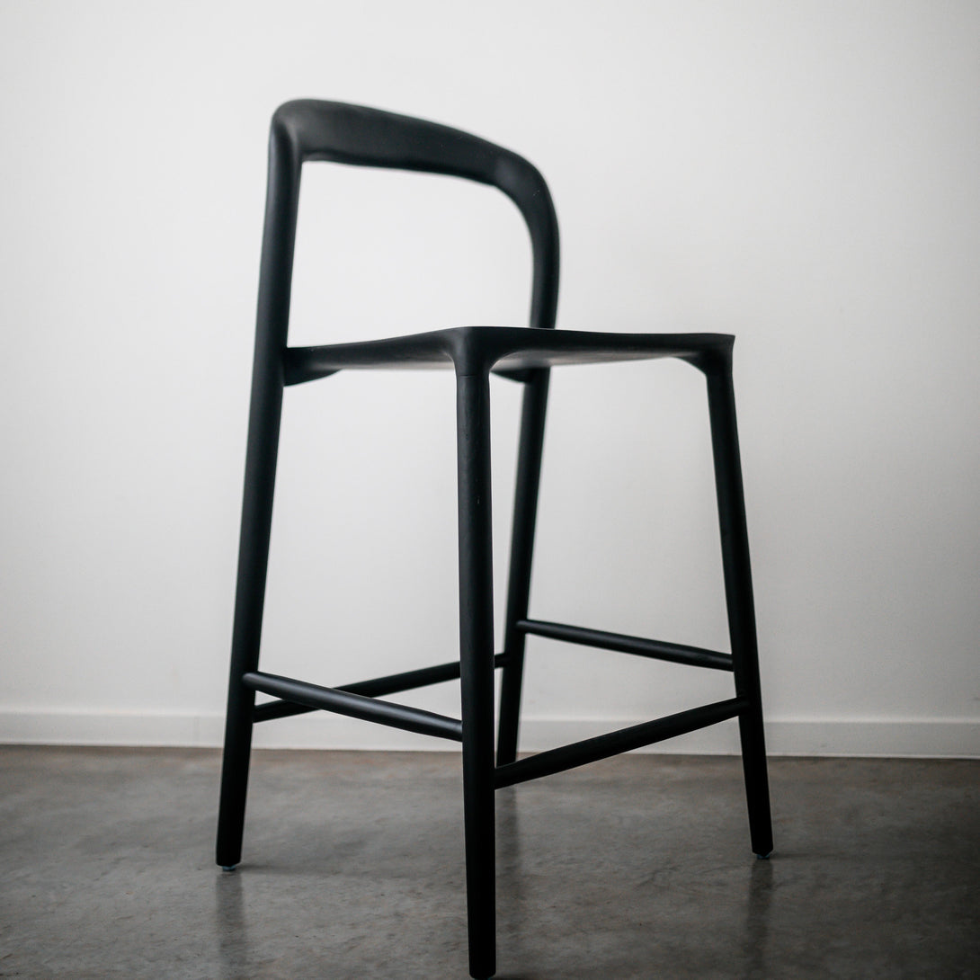 Black Mowelli Nora bar stool on a concrete floor – minimalist Belgian design barstool