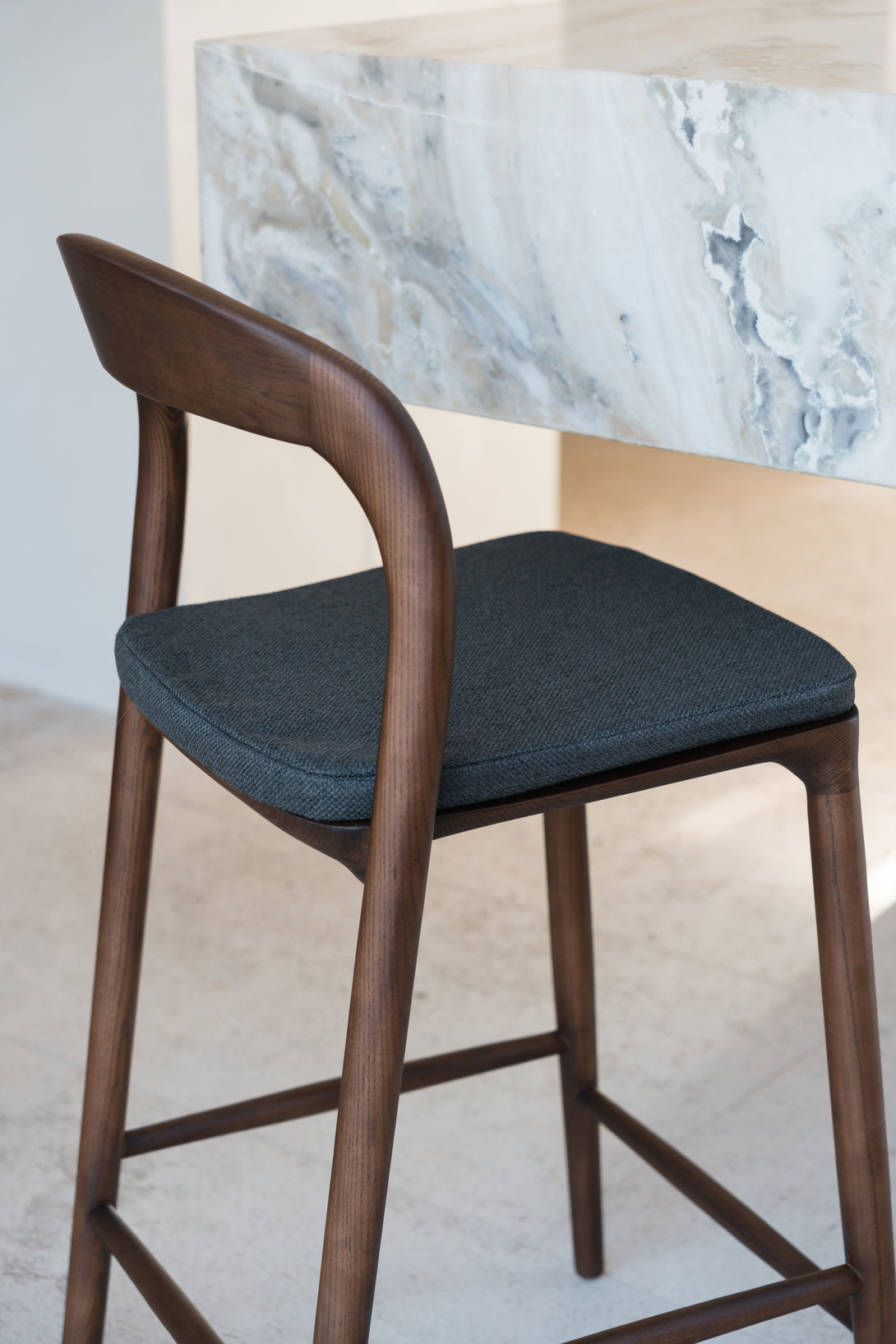 A charcoal black fabric pillow on a Nora walnut bar stool by Mowelli