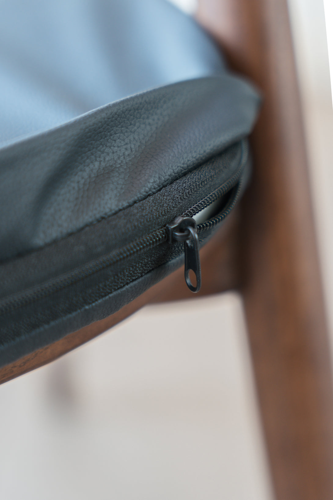 Close-up of a black leather pillow featuring the zipper to show that the pillow can be taken out of the cushion.