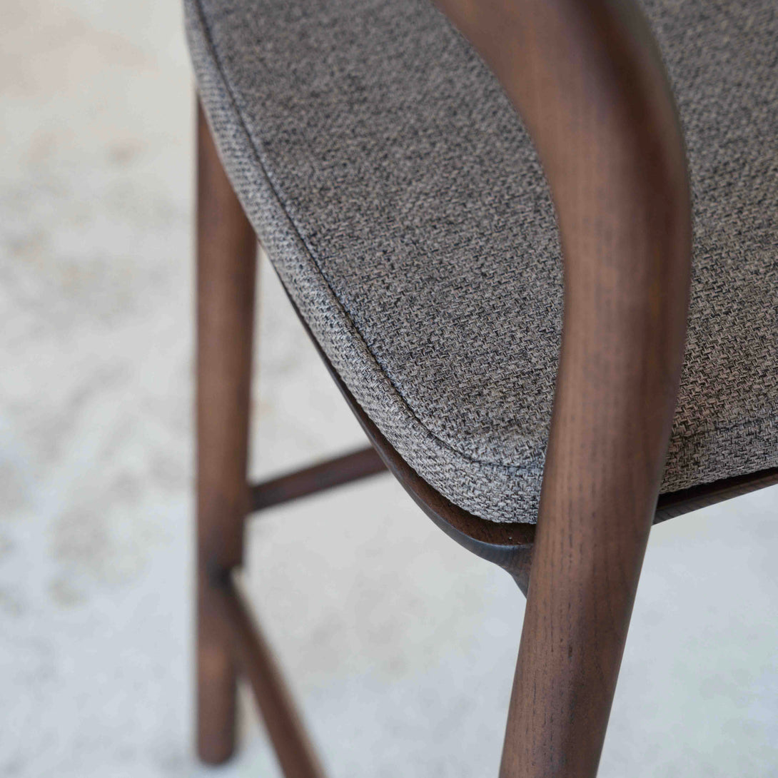 A close-up of a Nora bar stool with a mocha brown fabric pillow. 