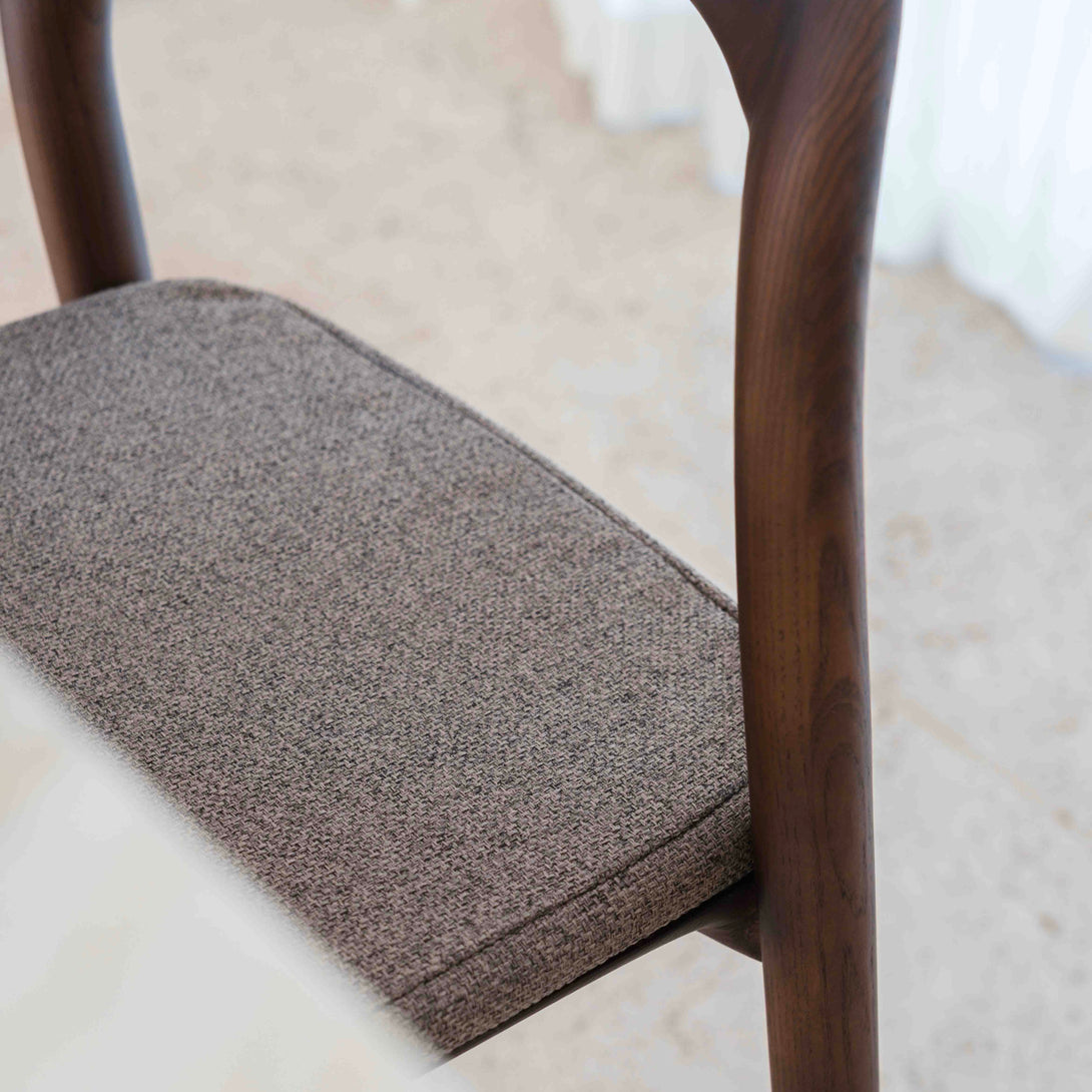 Close-up of a mocha brown fabric pillow laying on the Nora walnut bar stool by Mowelli