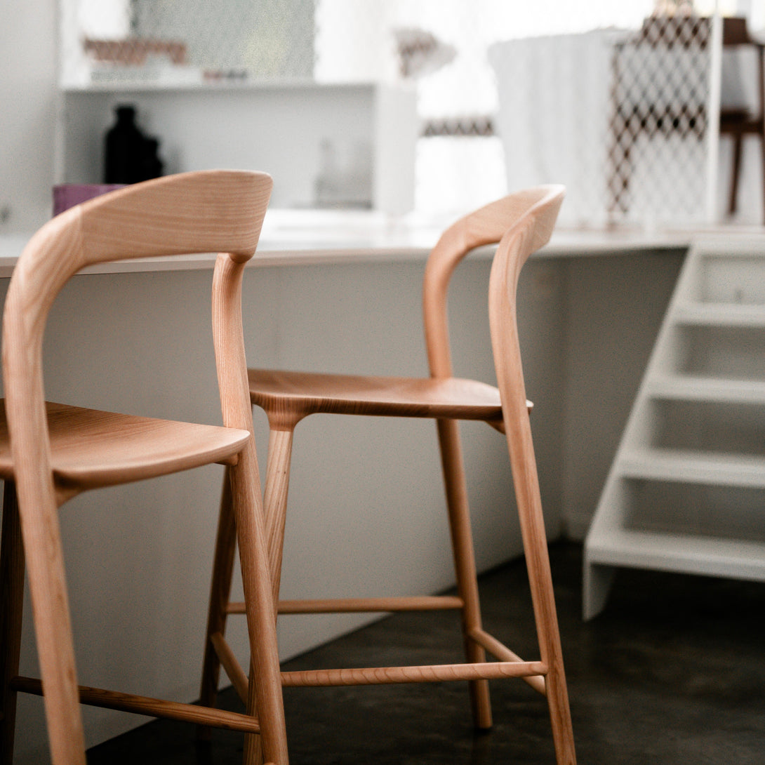 Side view of two ash wood Nora bar stools by Mowelli in a modern kitchen – contemporary wooden bar chairs