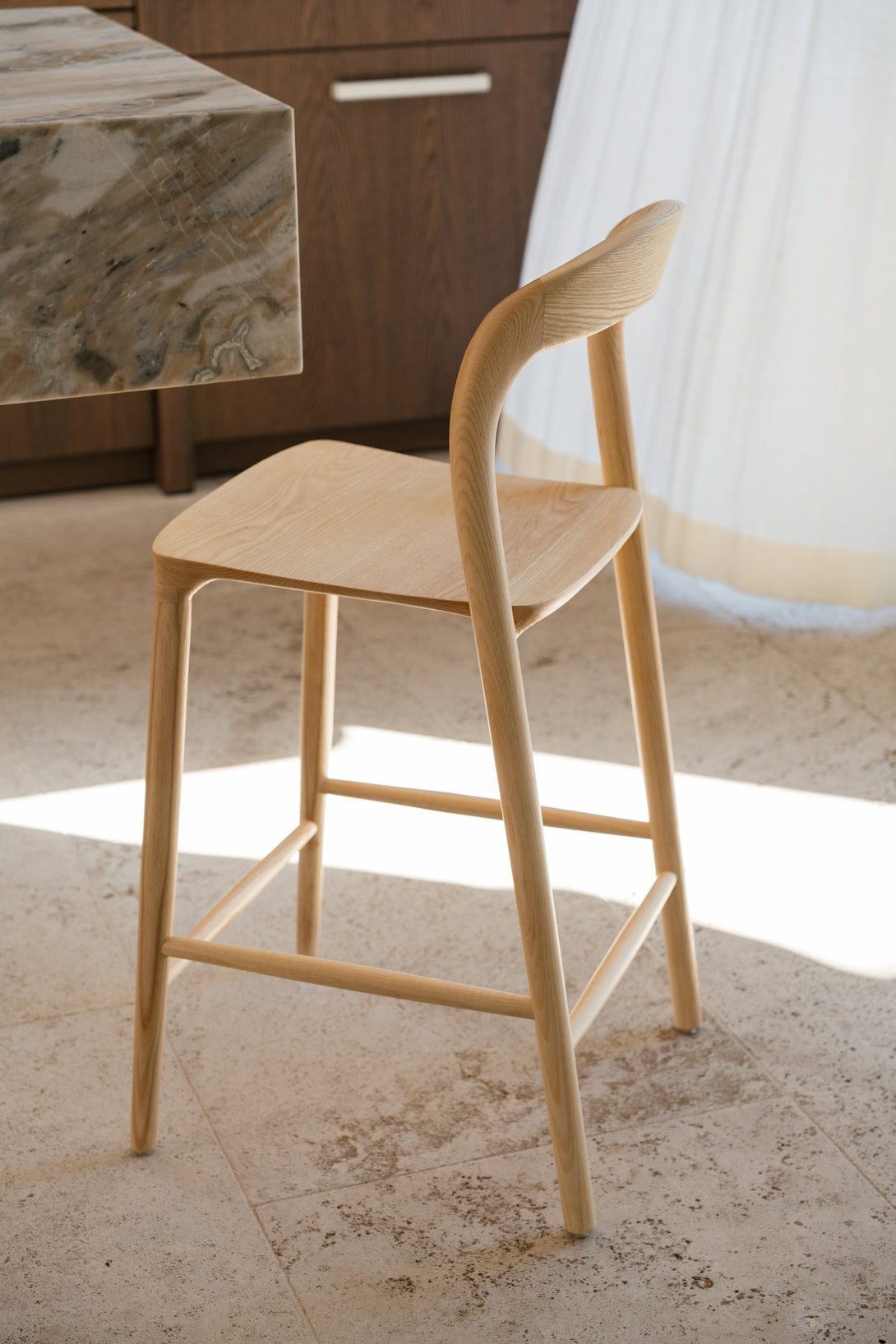 A natural Nora bar stool by Mowelli standing at a kitchen island 