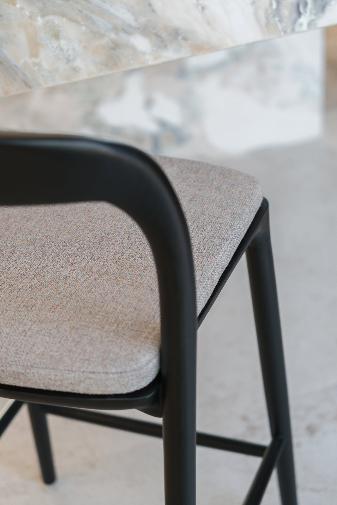 The back view of a soft greige pillow laying on a black Nora bar stool by Mowelli
