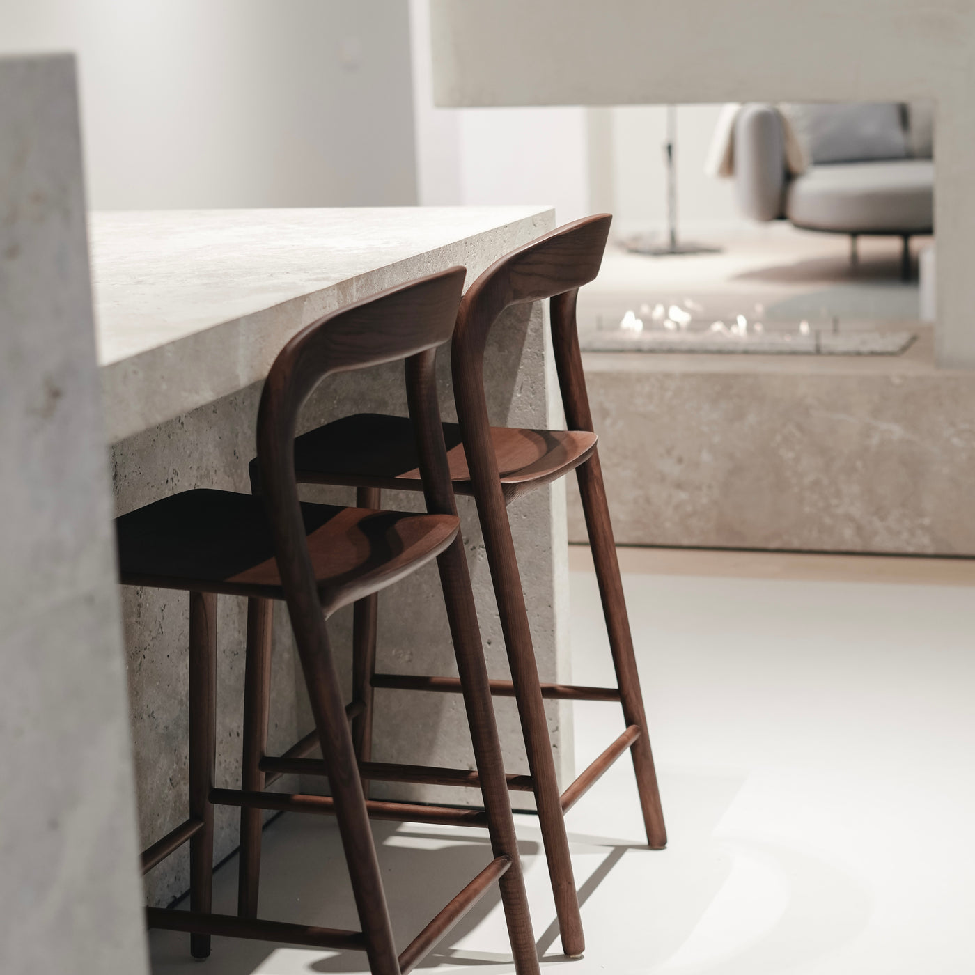 Two walnut Nora bar stools lined up at a concrete kitchen island – designer wooden bar chairs from Belgium