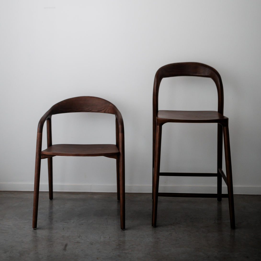 Walnut Nora bar stool next to its matching Nora dining chair on concrete floor – Mowelli Belgian wooden chair set