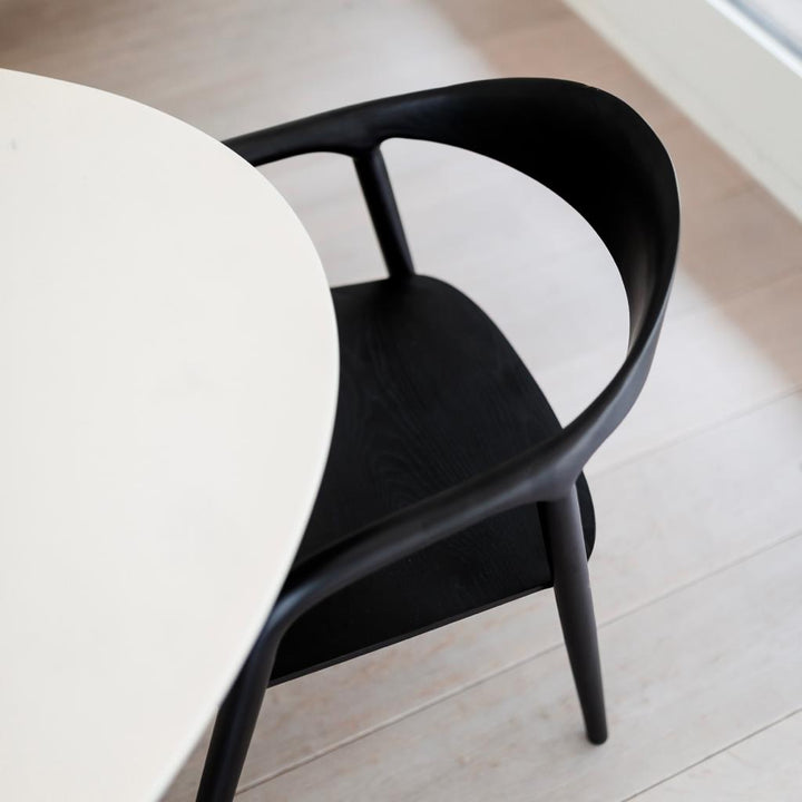 Black ash version of the Mowelli Nora dining chair viewed from above at a white dining table.