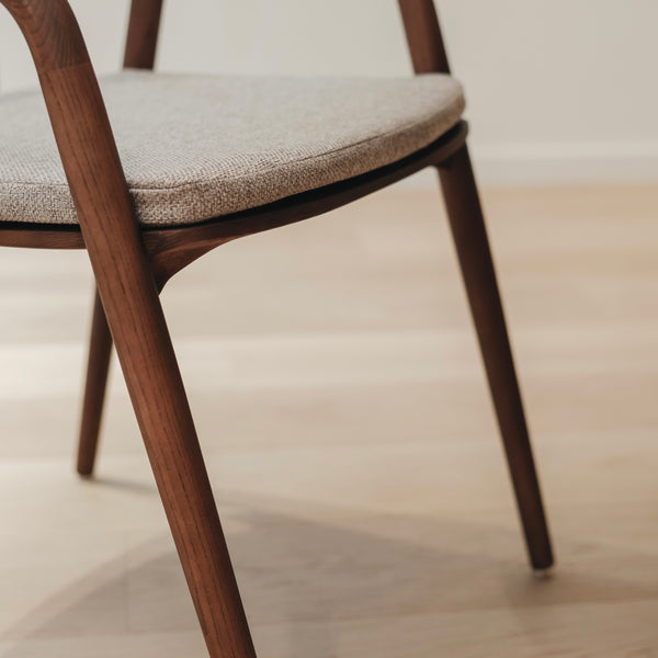 A close-up image of a Nora walnut dining chair with a soft greige cushion on its seat.