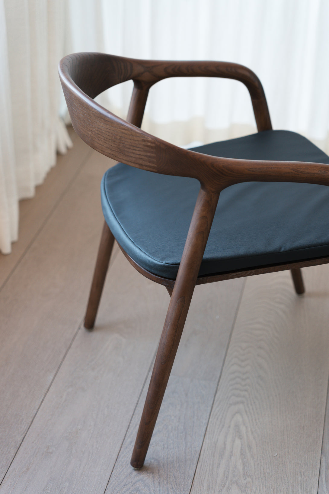 A walnut Nora dining chair with a charcoal black leather seat 