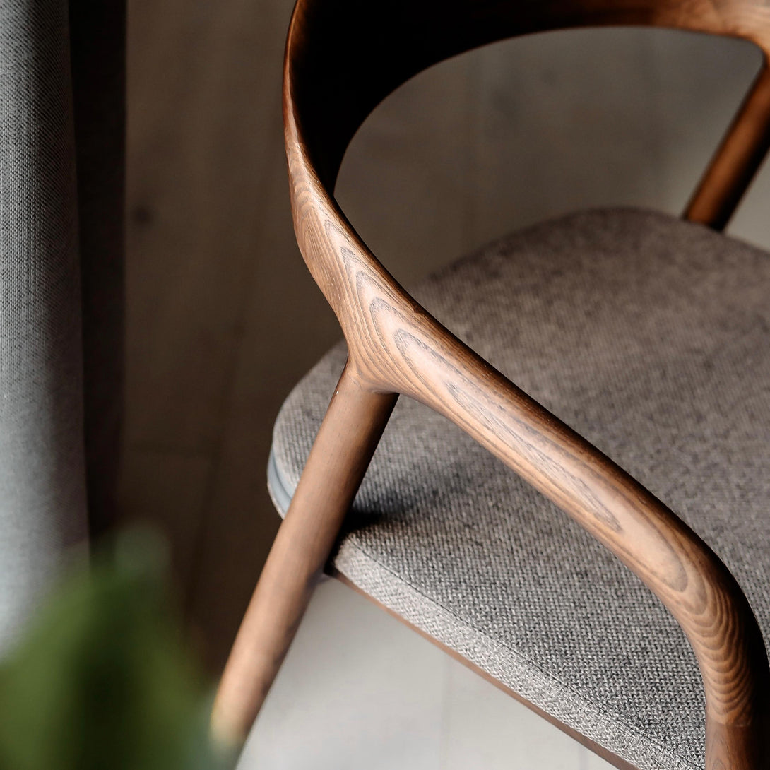 A close-up of a Nora walnut dining chair with a mocha brown pillow
