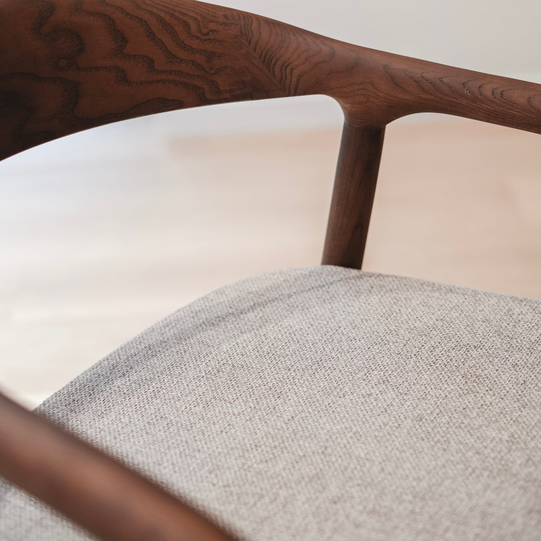 A close-up of a soft greige fabric seat on the Nora walnut dining chair by Mowelli