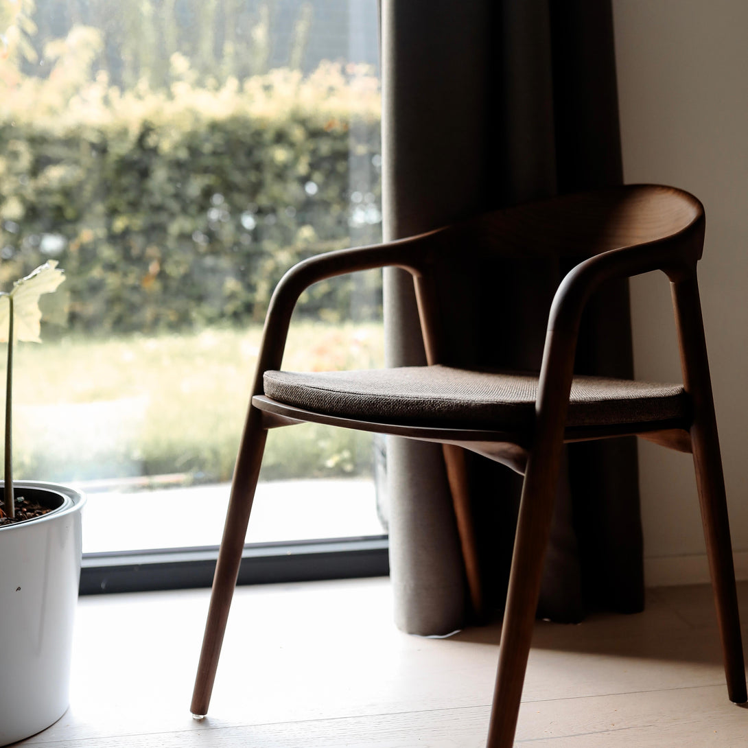 A Nora walnut dining chair standing by the window with a mocha brown fabric seat